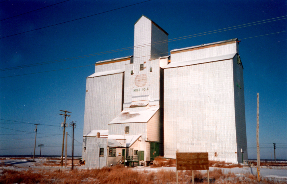 In 1962, an elevator was built by Federal Grain at Mile 10.6 along Wilkes Avenue on the outskirts of Winnipeg (known in the 1930s as the St. Charles Siding). Initially accompanied by a single crib annex, its capacity was expanded with a second annex in 1965, raising its total to 155,000 bushels. Sold to Manitoba Pool in 1972, a local management committee was formed in February 1973. Major renovations were undertaken in early 1988. The elevator closed around 2000, shortly before this photo was taken, and was demolished in early 2003.