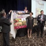 The new cover of the Real Dirt on Farming was unveiled at the Farm & Food Care Harvest Gala last week. Doing the unveiling was Farm & Food Care chair Brian Gilroy, left, Christine Schoonderwoerd, vice chair, and representing funder Wallenstein Feed & Supply Ltd., Pierre Petelle, president of CropLife Canada. Farm & Food Care Executive Director Kelly Daynard is at the podium.  Photo courtesy Farm and Food Care.
