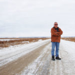 Barry Janssens stands on a road near his farm. At one time, the road would have cut through fields. Now it’s more of a causeway through a swamp.