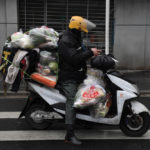 A delivery worker checks his mobile phone on an electric bike filled with vegetables on a street in Wuhan in China’s Hubei province on Feb. 28.
