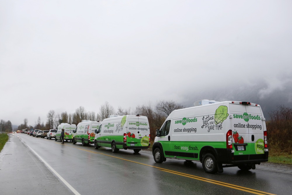 Delivery vans from the Save-On-Foods grocery store chain wait for a police escort to cross through a landslide near Hope, B.C. on Nov. 18, 2021 to restock the local grocery store after rainstorms caused flooding and landslides in the region. (Photo: Reuters/Jesse Winter)
