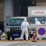 Chinese workers in protective suits are seen at a checkpoint on a road leading to a village near a farm where African swine fever was detected, Nov. 23, 2018.