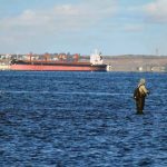 Fishermen are seen against a bulk carrier entering the port of Odesa under the grain initiative, in Odesa, southern Ukraine.