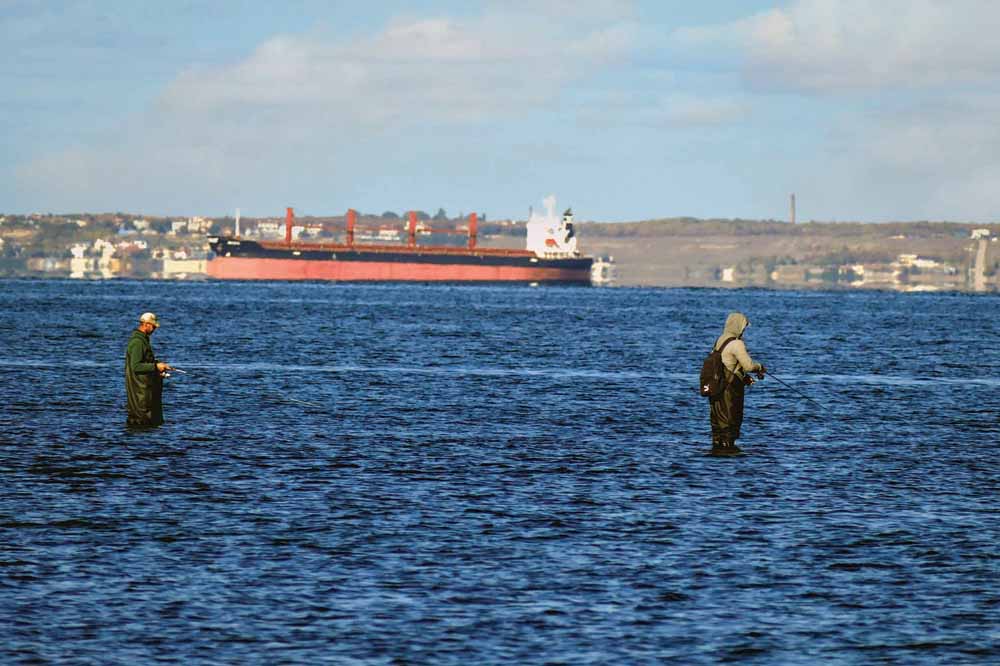 Fishermen are seen against a bulk carrier entering the port of Odesa under the grain initiative, in Odesa, southern Ukraine.