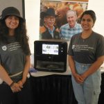 Kashika Sethi (l) and Rhea Thomas Thommana (r) were at Ag in Motion to represent food scientists Drs. Martin Reaney and Michael Nickerson and their 3D printer projects, including their work on printable protein-based materials, such as the pea-based “chicken leg” seen in the machine. (Becky Zimmer photo)