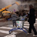 A woman, with her child, pushes a shopping trolley past a supermarket blocked by French farmers who dump tires and slurry as part of their protest over price pressures, taxes and green regulation, grievances shared by farmers across Europe, in Bon-Encontre near Agen, south of France, January 25, 2024. REUTERS/Nacho Doce