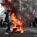 A man carries a Polish flag next to burning tyres, as farmers protest outside Polish Prime Minister Donald Tusk’s office against the European Union’s Green Deal and imports of Ukrainian agricultural products, in Warsaw, Poland, March 6, 2024. REUTERS/Kacper Pempel