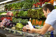 A man with a grocery cart walking down the produce isle.