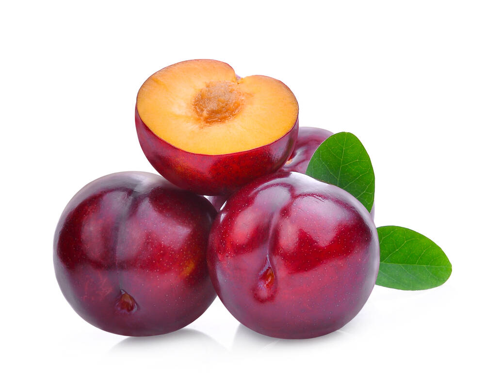 Whole and half of cherry red plum with green leaves isolated on white background.