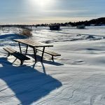 Snow drifts along the edge of Minnedosa Lake in western Manitoba while ice fishing huts can be seen in the background.