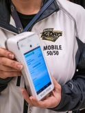 A woman holds a PDA , wearing a jacket with "mobile 50/50" and the Manitoba AgDays logo.