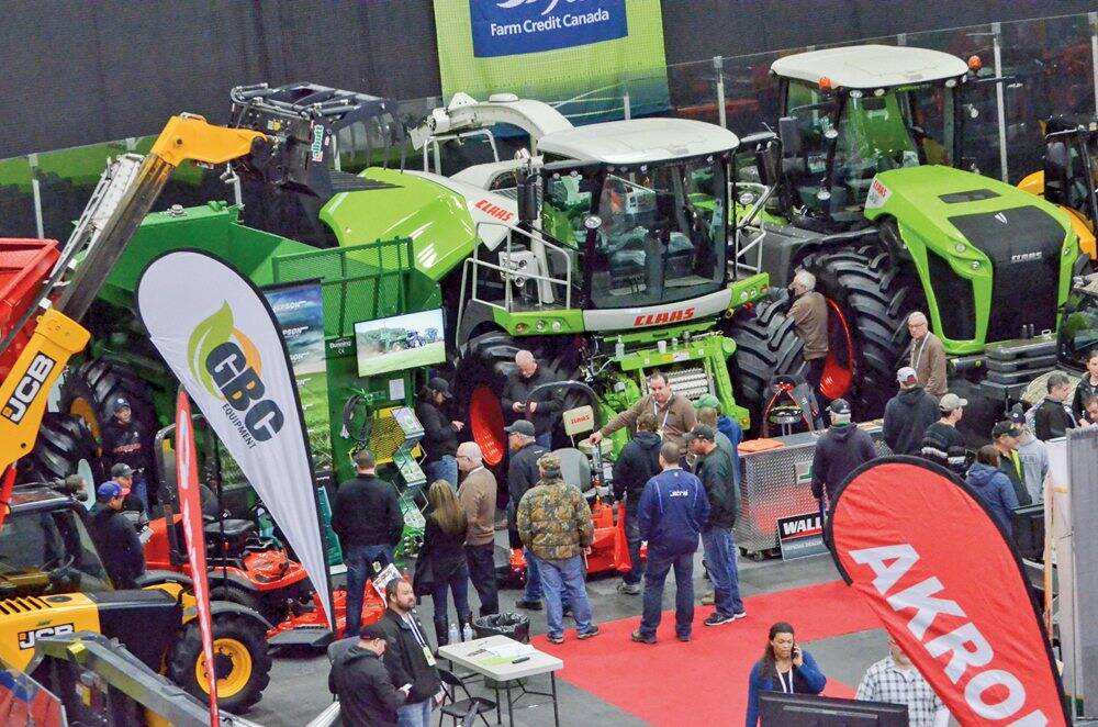 A diverse group of individuals gathered around large tractors, engaging in conversation and observation.