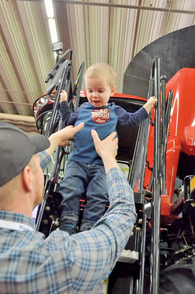 A man assists a small child as they step down from a red tractor