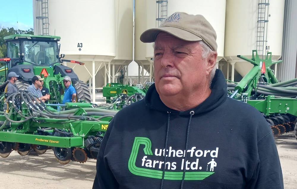 A man wearing a black hoodie with the logo "Rutherford Farms Ltd." stands in front of agricultural machinery.