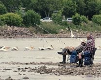 A person fishing from shore while seated, relaxing, in a chair.