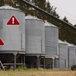 Farmers loading grain into a row of grain bins with safety warnings in risky areas.
Photo: AJ_Watt/istock/getty images