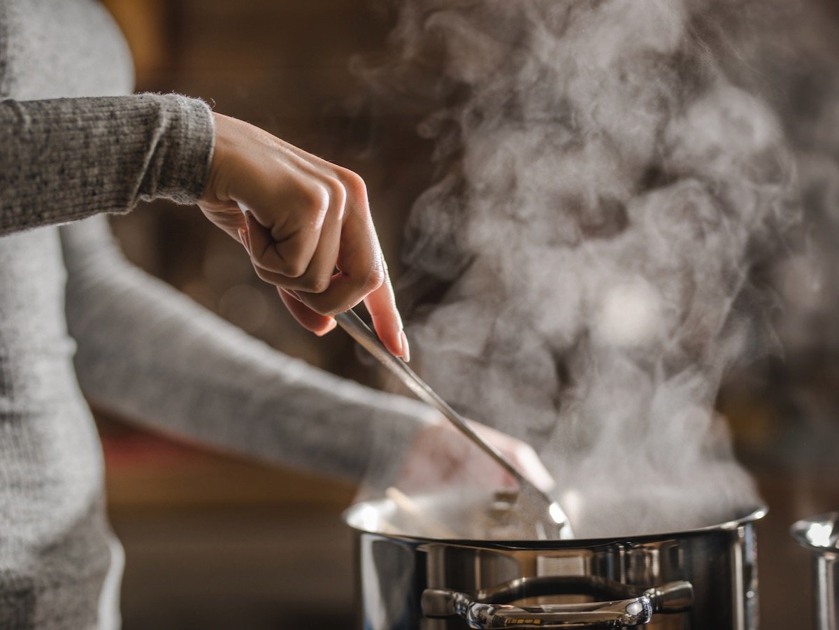 Unrecognizable woman stirring soup in a saucepan while making lunch