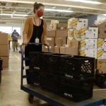 a worker pushes a cart loaded with crates in a community food bank warehouse