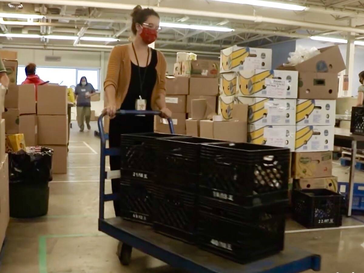 a worker pushes a cart loaded with crates in a community food bank warehouse