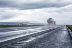 A speeding semi tractor dry bulk commodity trailer truck splashes and kicks up foggy water and sloppy haze, while an eastbound tandem trailer semi-truck passes in the opposite direction. Photo: Getty Images Plus