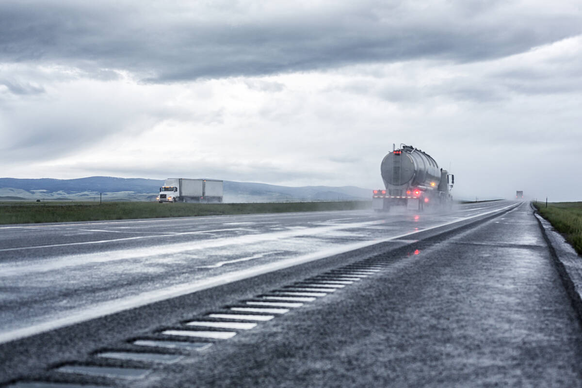 A speeding semi tractor dry bulk commodity trailer truck splashes and kicks up foggy water and sloppy haze, while an eastbound tandem trailer semi-truck passes in the opposite direction. Photo: Getty Images Plus