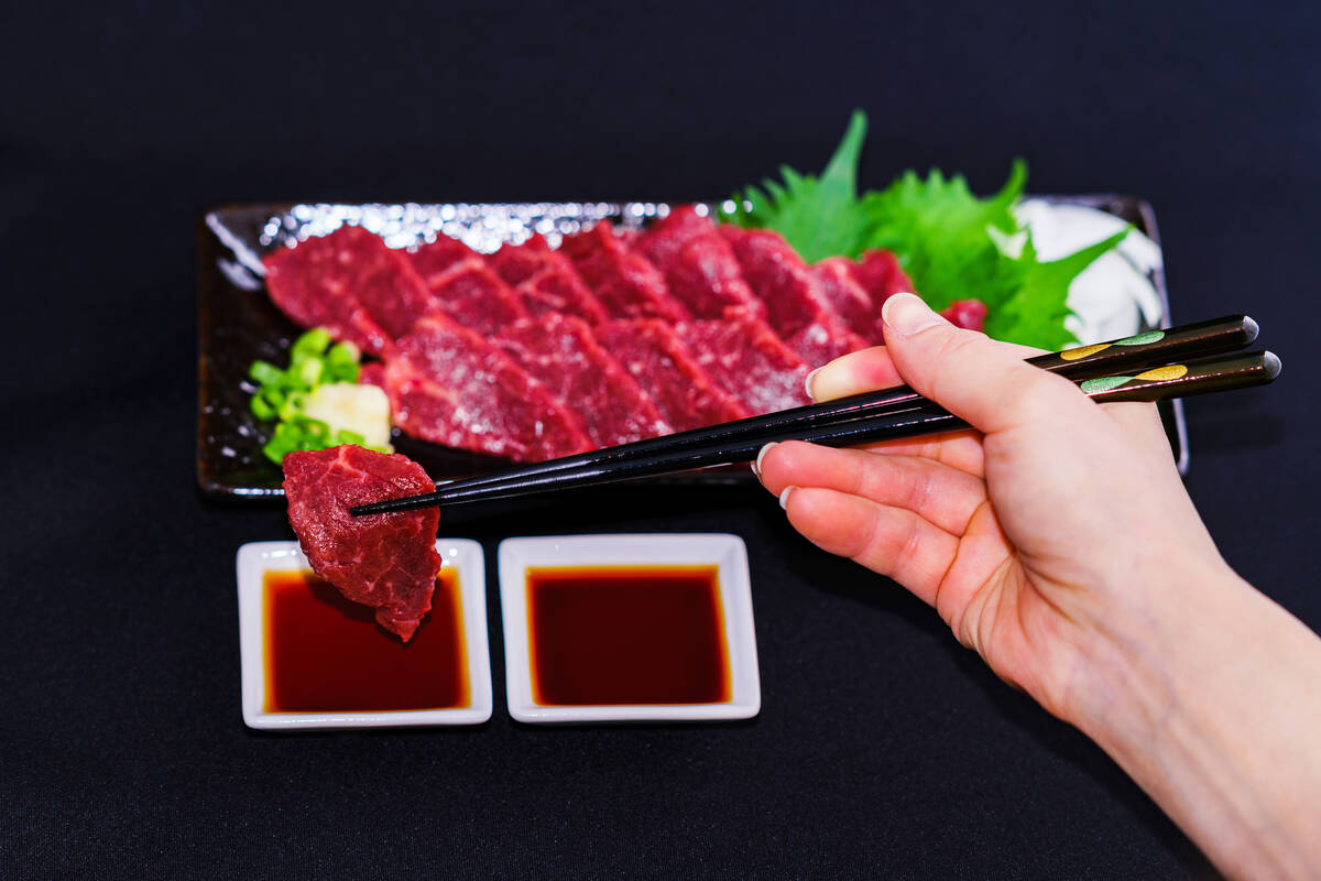 A hand picks up basashi (raw horse sashimi) with chopsticks. Photo: Show999/iStock/Getty Images
