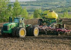 Green tractor pulling a fertilizer applicator through a field in rural Manitoba.