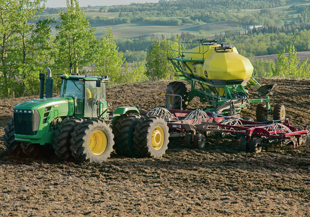 Green tractor pulling a fertilizer applicator through a field in rural Manitoba.