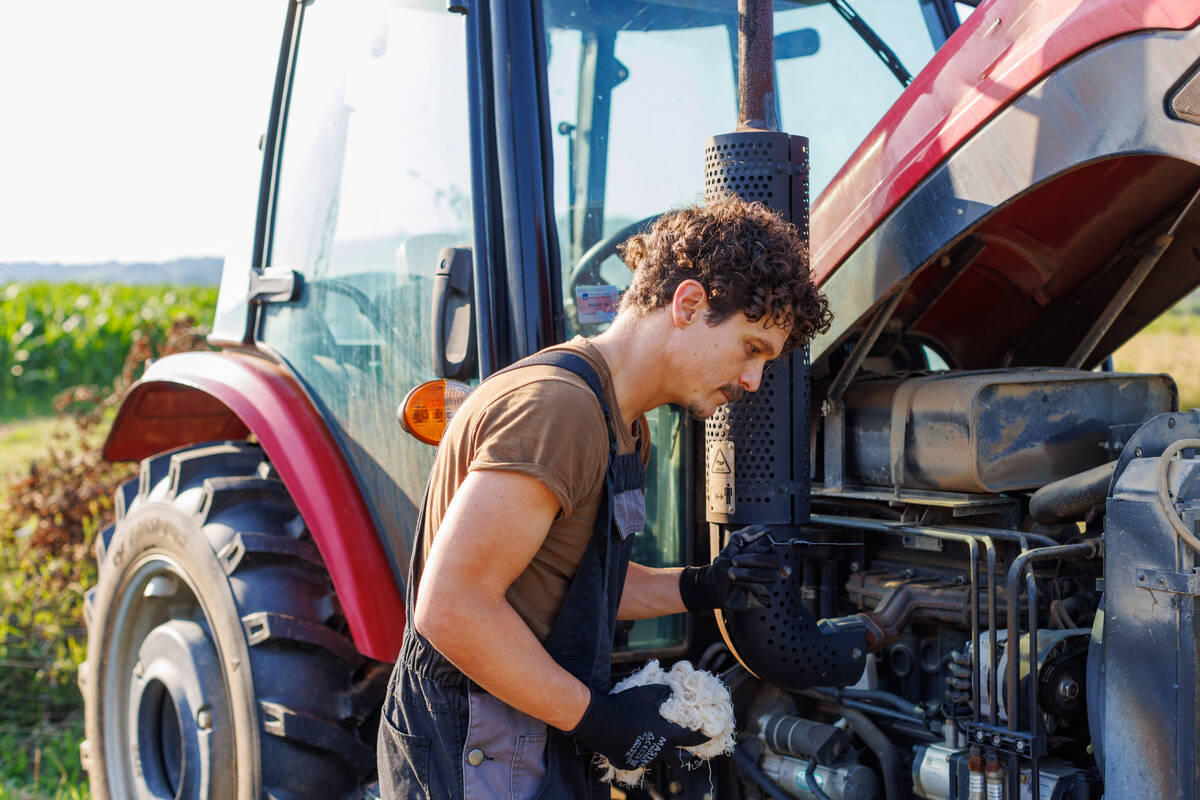 A young man in a farm field working on the engine of a red tractor on a clear day. Photo: vgajic/Getty Images