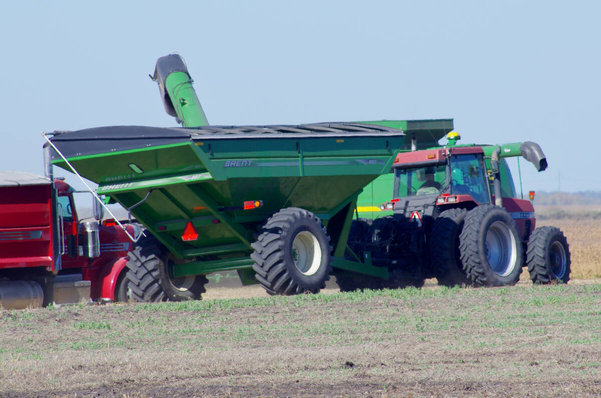 Red tractor and green Brent grain cart beside combine harvester in farm field. Photo: Alexis Stockford