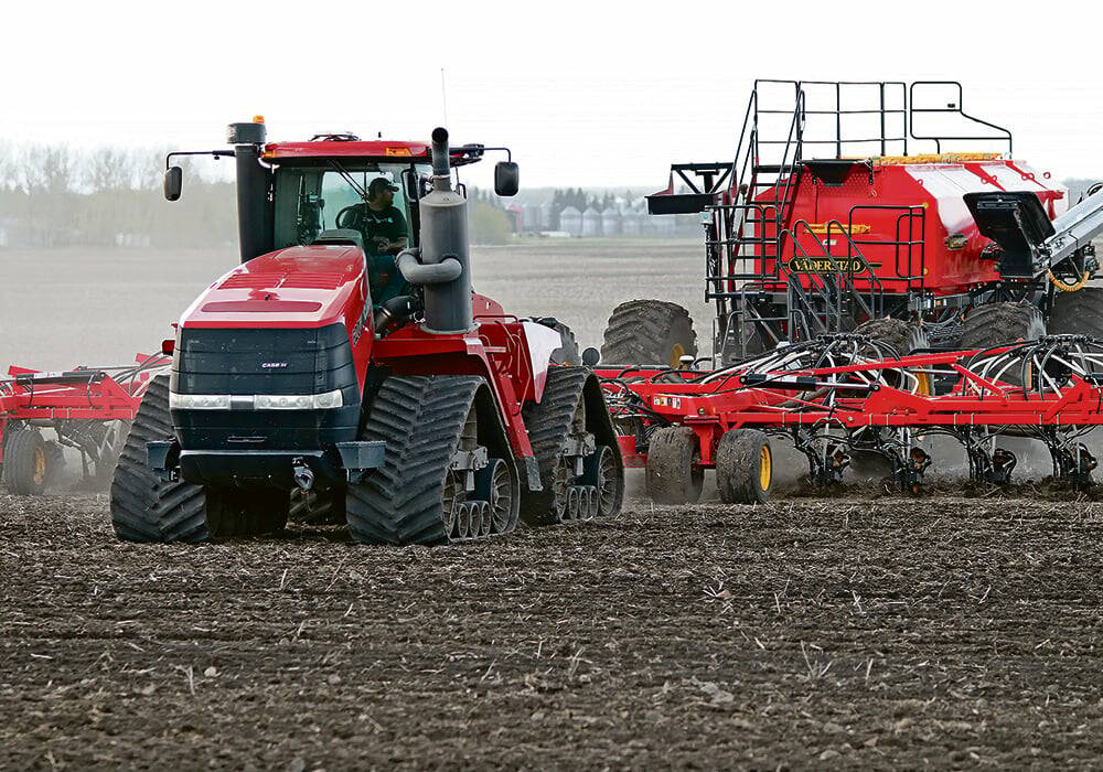 A red tractor pulls a planter across a Western Canadian field during spring seeding when fertilizer prices are a key cost factor. Photo: file.