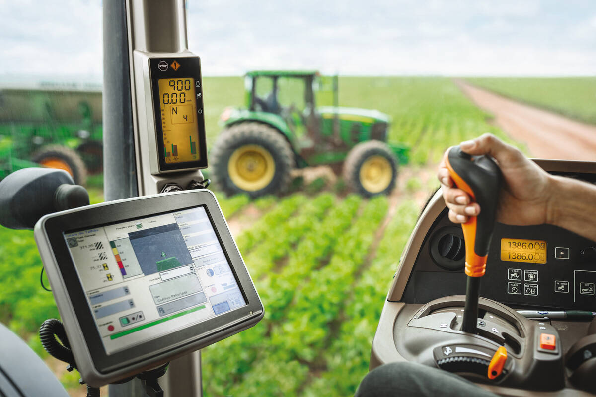 View from inside a tractor cab with a hand on the gear shift and a digital display screen showing field data during precision agriculture operations. Photo: Bayer AG