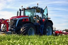 Operator climbing into a Massey Ferguson 9S.425 tractor in a green crop field with red implements attached.