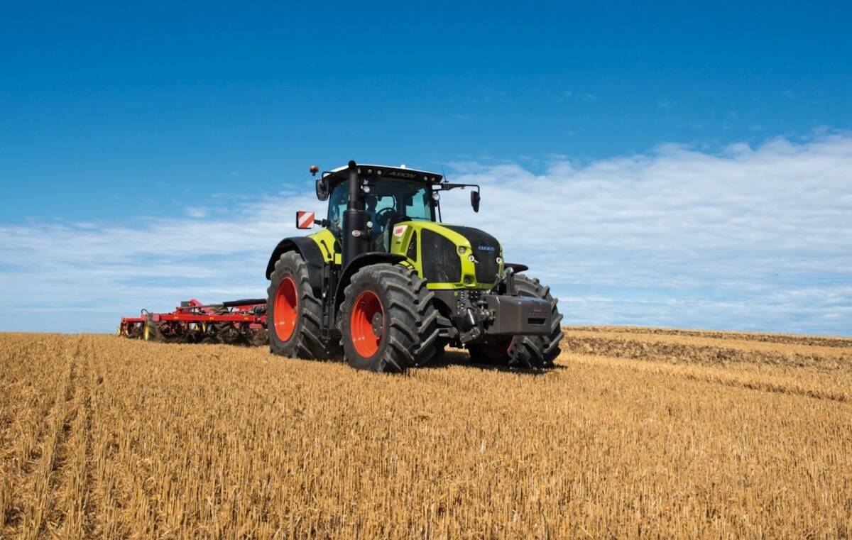 Yellow-green Claas Axion tractor pulling red tillage equipment through stubble under a blue sky.