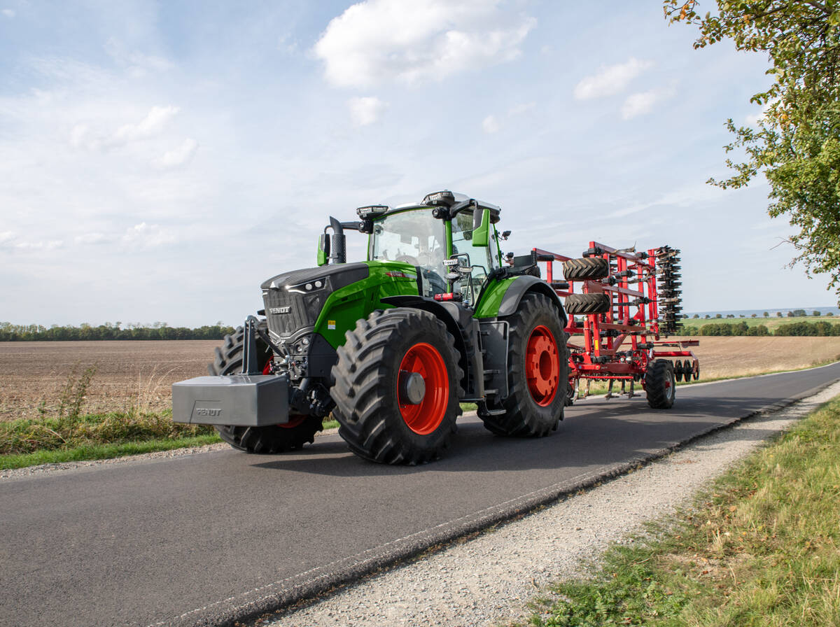 Green and red Fendt 1000 Vario Gen4 tractor transporting a folded cultivator on a paved road. Photo: Agco