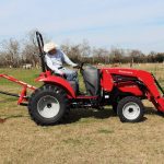 Operator using a red Mahindra 1533 compact tractor with front loader and post-hole auger on a rural property. Photo: PRNewsFoto/Mahindra.