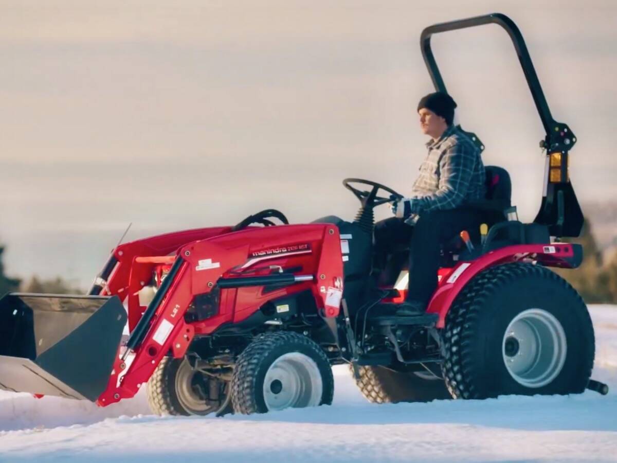 Operator driving a red Mahindra utility tractor with front loader attachment through snow. Photo: Screen Capture/MAGNA via YouTube.