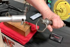 A hand holding the Drawhand tool bar with a specially designed hitch pin attached, displayed at a trade show booth, demonstrating the farm safety tool's connection mechanism. Photo: Greg Berg