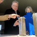 Under the direction of Heather White, Soils at Guelph, far left, Ontario Senator Rob Black, centre, and Yukon Senator Pat Duncan, right, compare the integrity of two soil samples gently laid in mesh baskets to see which will hold its form and which will crumble in long tubes of still water. Photo: Diana Martin