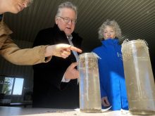 Under the direction of Heather White, Soils at Guelph, far left, Ontario Senator Rob Black, centre, and Yukon Senator Pat Duncan, right, compare the integrity of two soil samples gently laid in mesh baskets to see which will hold its form and which will crumble in long tubes of still water. Photo: Diana Martin