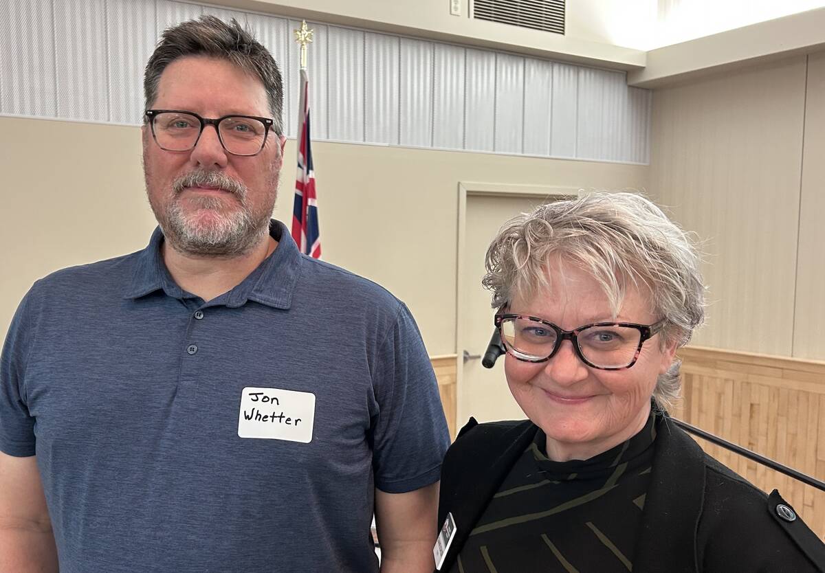 Jon Whetter wearing a name tag and Dianne Kohler in glasses standing side by side at an indoor event, with a Manitoba flag visible in the background. Photo: Gord Gilmour