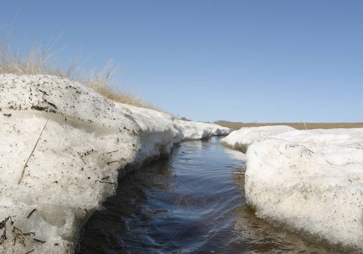 Spring meltwater flowing through a narrow channel between thick snowbanks in an open Prairie landscape. Photo: file