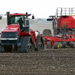 A red Case IH Steiger tractor pulling a Bourgault air seeder across a bare Prairie field in spring seeding conditions. Photo: file