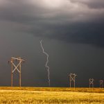 A lightning bolt strikes near a row of wooden power line poles crossing a golden Prairie field under a dark storm sky. Photo: Bobloblaw/iStock/Getty Images