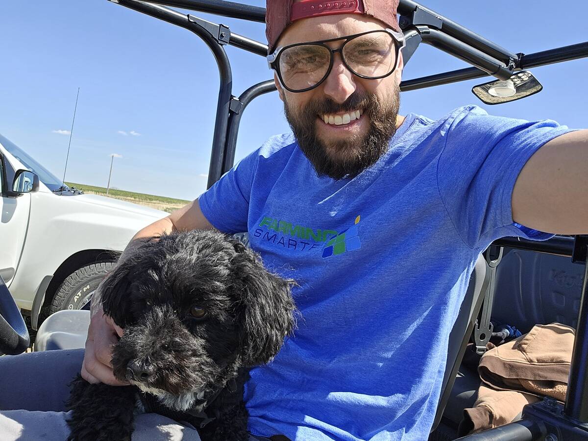 Mike Gretzinger, researcher with Farming Smarter, holds a black dog while sitting in a utility vehicle in a field. Photo: Mike Gretzinger