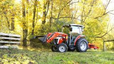 A red Massey Ferguson compact tractor with front loader operates in a field surrounded by foliage, illustrating spring equipment readiness ahead of the busy season.