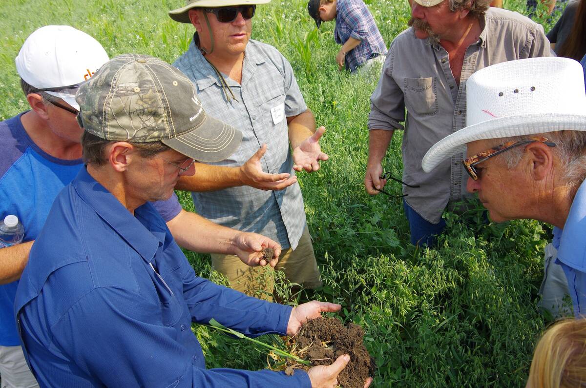 A farmer holds a clump of dark prairie soil during a soil health field tour near Pierson, Man., in 2018, as other attendees look on. Photo: Alexis Stockford