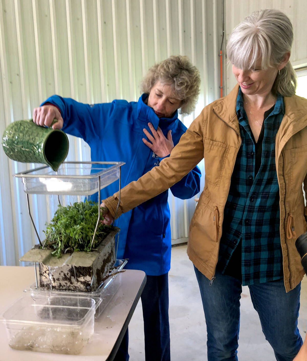 Two women conduct a soil water infiltration demonstration using a layered soil block and collection tray at an indoor agricultural event. Photo: Diana Martin